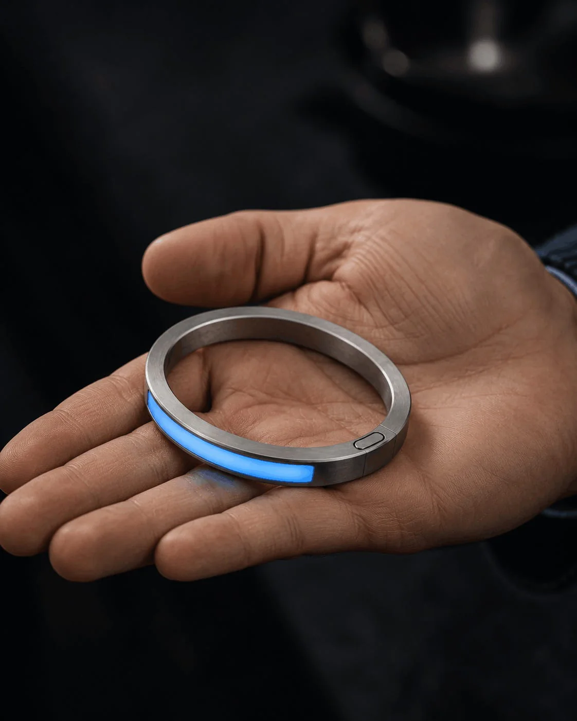 Blue-illuminated JUVEIL bangle resting in an open hand against a dark background.