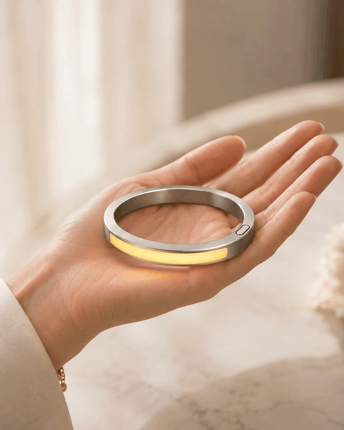 Yellow-illuminated JUVEIL bangle resting in an open hand in a bright setting.